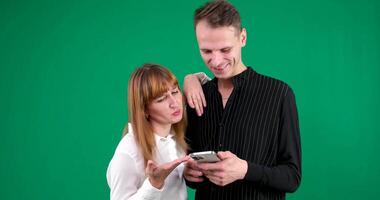 man and woman with gadgets tablet phone in hands on green background talking laugh holding meeting learning to work on Internet flirting relationships flirting couple solving issue positive emotions video