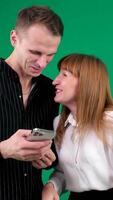 de Jeune couple en train de regarder marrant sur mobile téléphone, noir et blanc vêtements, verticale , posant sur isolé vert Contexte video
