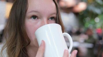 une beau, sucré fille est assis seul et les boissons thé ou café de une tasse. inhaler le arôme de le boire. elle regards très calme et paisible video