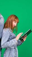 Confident red-haired female consultant in denim clothes using tablet touch screen, standing on green background video