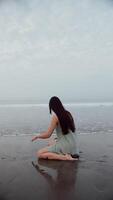 niña sentado en el agua en el océano, negro playa con ondas. video