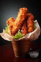 Deep fried chicken drumsticks in a clay pot on a black background photo