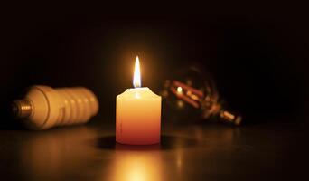 A white burning candle in close-up on a black surface against two bulb lights in black background photo