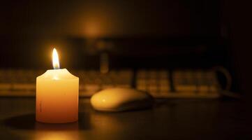 A white burning candle in close-up on a desk against a computer out of focus in black background photo