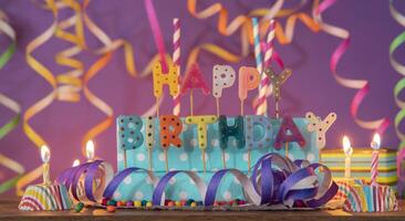 Letters of different colors forming the phrase HAPPY BIRTHDAY, with lit candles against purple out-of-focus background photo