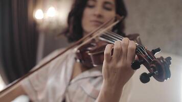 beautiful girl playing the violin while sitting on the bed at home, hand-held shooting, close-up video