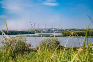 río divisor verde pueblo y fábrica con grande emitiendo chimeneas foto