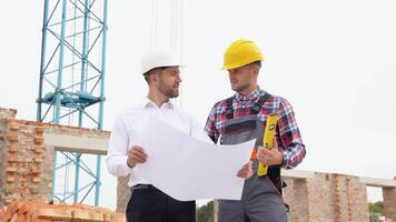 Two specialists inspect commercial, industrial building construction site. Real estate project with civil engineer. In the background crane, skyscraper concrete formwork frames video