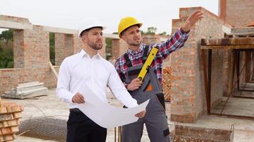 dos construcción trabajadores Mira a un arquitectónico dibujo en casa construcción video