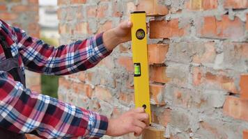 trabajador controlar ladrillo pared utilizando nivel herramienta, cerca arriba video