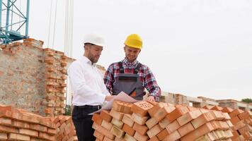 Two construction workers look at an architectural drawing in house construction video