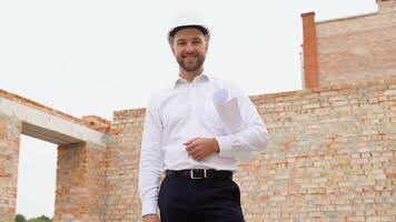 retrato de satisfecho y confidente ingeniero o inversor con casco y documentos en edificio sitio video