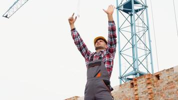 sérieux directeur dans casque et uniforme donnant commandes à grue opérateur. barbu homme faire des gestes et en criant pendant travail processus video