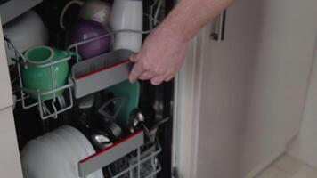 Young man loading dirty dishes into a dishwasher machine. A man uses modern appliance to keep the home clean. Close-up, top view video