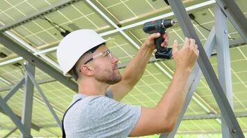 Male engineer in protective helmet installing solar photovoltaic panel system using screwdriver. Alternative energy ecological concept video