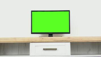 Empty living room at home with chroma key placeholder on monitor. Stylish apartment interior with TV set with green screen mock up gisplay standing on television stand. Zoom on shot video