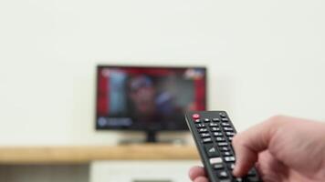 Man's hand selects internet tv channels with remote control, close-up. Person controls TV using a modern remote control. A man watches smart TV and uses black remote control video