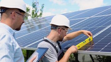 Two workers in helmets check the installed solar panels. Green electricity and alternative energy ecological concept video