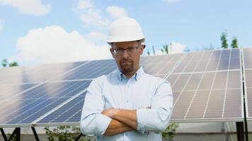 Close up portrait of male worker in protective helmet standing near solar panel. Portrait of confident engineer of solar cell farm industry. Staff confident pose Solar cell panel installation video