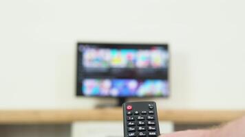 Man's hand selects internet tv channels with remote control, close-up. Person controls TV using a modern remote control. A man watches smart TV and uses black remote control video