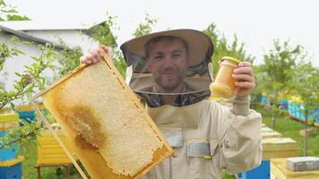 Beekeeper holding a honeycomb frame and jar with honey. Beekeeping concept. Beekeeper harvesting honey video