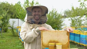 Portrait of beekeeper with a honeycomb frame and jars with honey. Beekeeping concept. Beekeeper harvesting honey video