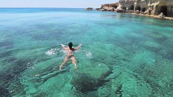 Tourist swim in Northern cyprus Ayia napa bay shore with cystal clear blue mediterranean waters and tranquil seascape and rocky stone shore. Sea caves popular travel destination video