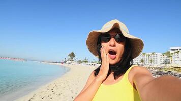 Young caucasian traveler tourist or influencer take selfie in sunny beach.Mouth cover beach pose surprised shocked being silly on vacation pose social media stories fun me time video