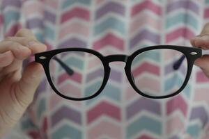 Hand holding glasses in optical store, eyeglasses in hand photo