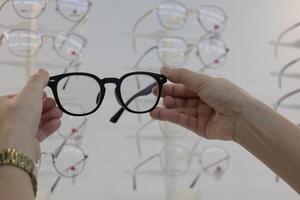 Hand holding glasses in optical store, eyeglasses in hand photo