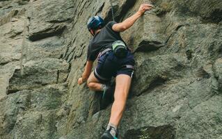 Young man in equipment doing rock climbing outdoors. Training area for outdoor activities. Extreme sport. photo