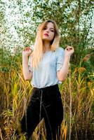 Beautiful young girl wearing blank gray t-shirt and black jeans posing against high green and yellow grass in early warm autumn. Outdoor portrait of beautiful female model photo