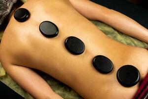 Black hot basalt stones are laid out on a woman's back. Massage procedure. Therapist relieves stress from client's sore spots. Spa treatments. photo