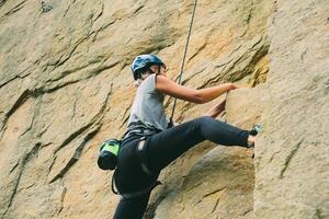 Young athletic woman in equipment doing rock climbing outdoors. Training area for outdoor activities. Extreme sport. photo