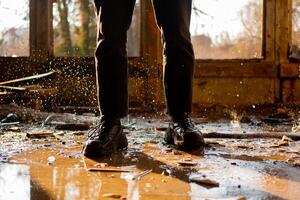 Male legs in black pants and sneakers among the puddle and frozen drops in a flooded, destroyed and abandoned house. Solar rays. Consequences of a natural disaster. photo