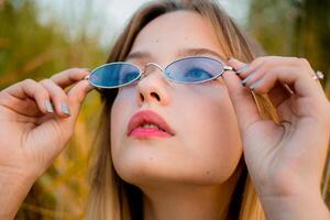 Beautiful young girl wearing blank gray t-shirt and black jeans in blue glasses posing against high green and yellow grass in early warm autumn. Outdoor portrait of beautiful female model. photo