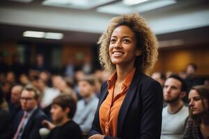 A woman standing confidently in front of a large crowd of people, who are listening attentively. photo