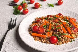 Salad with buckwheat and vegetables on a white plate photo