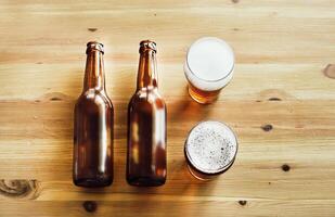 Two empty beer bottles, two glasses with beer on a wooden background photo