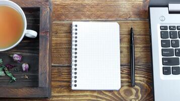 Wooden tray with a cup of herbal tea, a laptop and an open notebook photo