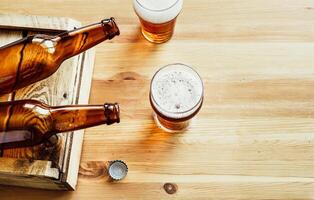 Two empty beer bottles, two glasses with beer on a wooden background photo