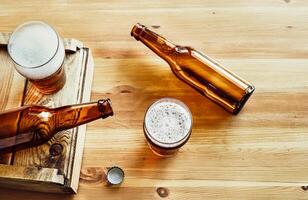 Two empty beer bottles, two glasses with beer on a wooden background photo