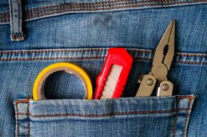 a pair of scissors and a pair of pliers in the pocket of a pair of jeans photo