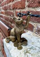 An artistic bronze cat figurine holding a pair of eyeglasses, surrounded by scattered coins on a stone ledge. photo