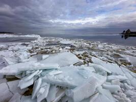 Crystalline ice sheets fracture and float on Russia's Lake Ladoga, capturing the stark beauty of spring's thaw under a clouded sky. photo