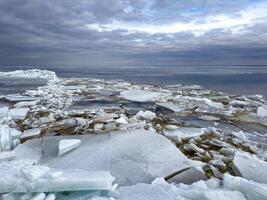 A dramatic expanse of broken ice sheets stretching to the horizon under a moody overcast sky, depicting a stark, cold arctic landscape photo