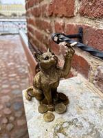 An artistic bronze cat figurine holding a pair of eyeglasses, surrounded by scattered coins on a stone ledge. photo