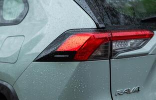 The back of a green toyota rav4 hybrid car with a sign or logo with raindrops in the park and the rear light close-up. Kyiv, Ukraine - April 2024 photo