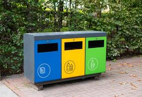 Three different garbage container for sorting waste in the park. Yellow for plastic, green for glass, blue for paper. Separating and sorting trash, concept pollution of the environment. photo