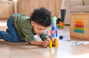 concentrado latinos chico jugando juguetes sentado en calentar piso en moderno vivo habitación. bebé desarrollo. pequeño torre. aprendizaje creativo concepto foto